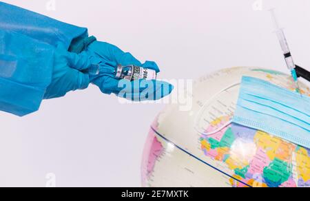 Ein vergrößertes Foto, in dem die Hände des Arztes eine halten Ampulle mit einem Coronavirus-Impfstoff und einer Spritze daneben Ein Globus und eine medizinische Maske auf einem weißen Stockfoto