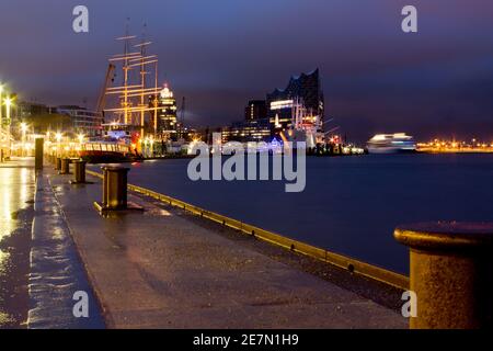 Ein ruhiger Blick auf den Hamburger Hafen bei Nacht, mit der beleuchteten Elbphilharmonie und den hohen Schiffen, die sich im Wasser spiegeln und die Stadt zur Schau stellen. Stockfoto