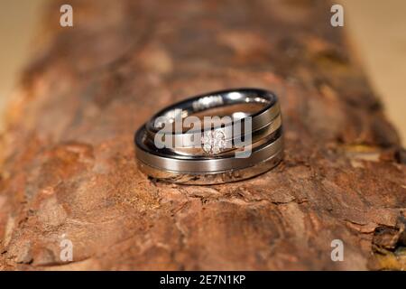 Eheringe – Ein Paar eleganter silberner Eheringe mit einem Diamantdetail auf rustikaler Rinde, das Liebe und Engagement symbolisiert. Stockfoto