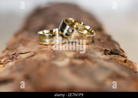 Eheringe – zwei elegante goldene Eheringe auf einer rustikalen Holzoberfläche, die Liebe, Engagement und zeitlose Schönheit symbolisieren. Stockfoto