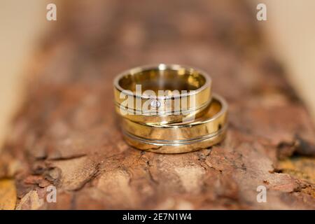 Eheringe – Nahaufnahme zweier goldener Eheringe auf einer strukturierten Holzoberfläche, die Liebe, Engagement und zeitlose Eleganz symbolisieren. Stockfoto