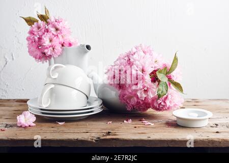 Weiße Tassen, Teekanne und rosa japanische Kirschblüten. Stillleben im Frühling. Stockfoto