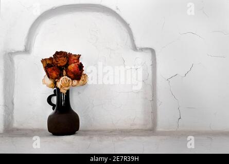 Trockene Rosen in einer Vase aus Keramik in der Wand Nische Stockfoto