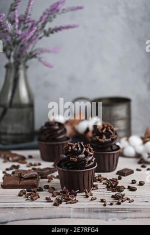 Mehrere Muffins oder Cupcakes mit schokoladenförmiger Sahne am weißen Tisch. Festliche Kerze brennt auf einem Schokoladenkuchen. Es gibt Schokolade Chips verstreut Stockfoto