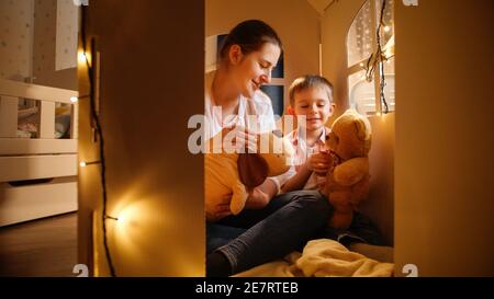 Netter kleiner Junge und junge Mutter spielen Spiele mit Spielzeug Teddybären in der Nacht im Zelt oder Spielzeughaus. Konzept des Spielens von Kindern und der Familie, die Zeit hat Stockfoto