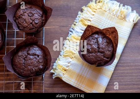 Schokoladen-Muffins in braunen Pappbechern auf Holzschneidebrett Stockfoto