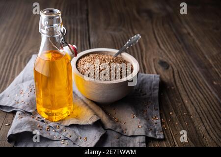 Leinsamenöl in einer Glasflasche, verziert mit ganzen Samen auf rustikalem Holzhintergrund mit Kopierraum Stockfoto