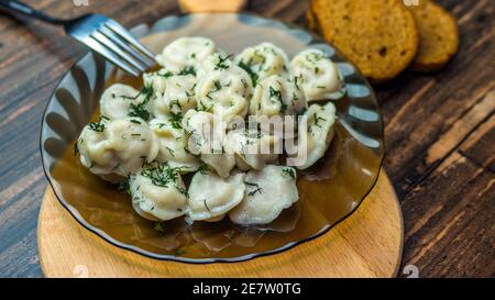 Knödel in einem Teller auf einem hölzernen Tablett, leckere hausgemachte Speisen, Knödel mit Kräutern verziert, russische Speisen, Knödel Kochen. Stockfoto