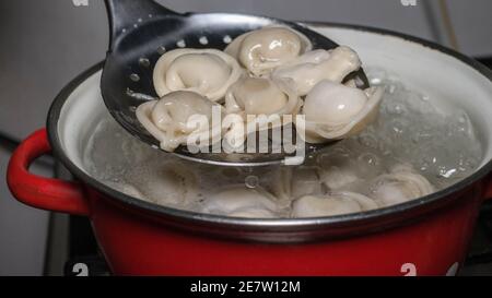 Bereiten Sie Knödel in einem Topf, rühren kochende Knödel mit einer speziellen Kugel, köstliche hausgemachte Speisen. Stockfoto