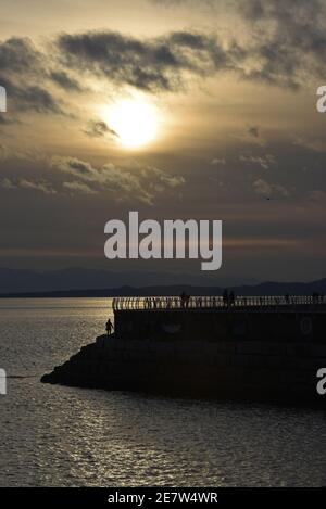 Silhouettierte Fußgänger laufen am Wellenbrecher Ogden Point bei Sonnenuntergang in Victoria auf Vancouver Island, British Columbia, Kanada entlang Stockfoto