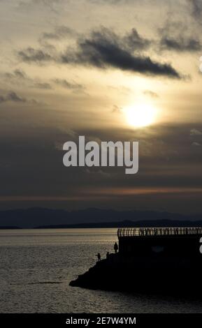 Silhouettierte Fußgänger laufen am Wellenbrecher Ogden Point bei Sonnenuntergang in Victoria auf Vancouver Island, British Columbia, Kanada entlang Stockfoto