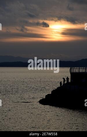 Silhouettierte Fußgänger laufen am Wellenbrecher Ogden Point bei Sonnenuntergang in Victoria auf Vancouver Island, British Columbia, Kanada entlang Stockfoto