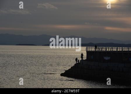 Silhouettierte Fußgänger laufen am Wellenbrecher Ogden Point bei Sonnenuntergang in Victoria auf Vancouver Island, British Columbia, Kanada entlang Stockfoto