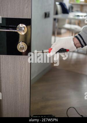 Ein Handwerker repariert Innentüren, ein Mann installiert ein Schloss an der Tür. Verwenden Sie einen Schraubendreher. Stockfoto