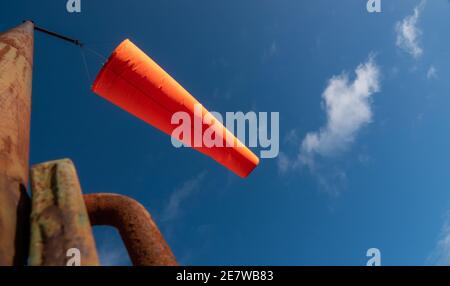 Eine große rot orange aufgeblasene Windsocke betrachtete Eisen Pol unter blauem Himmel Stockfoto