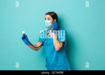 Covid-19, Pandemie- und Medizinkonzept. Bild einer schönen Ärztin in medizinischer Maske, Peelings und Handschuhe, Überprüfung der Patientin mit Stethoskop Stockfoto