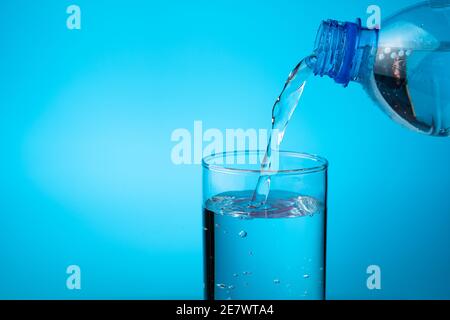 Ein Glas gefüllt mit Wasser aus einer Plastikflasche auf blauem Hintergrund. Stockfoto