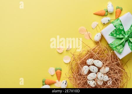 Wachteleier im Nest und Geschenkbox mit grünem Band auf gelbem Trendfarbe Hintergrund. Ostern minimale kreative horizontale Komposition mit Kopierraum. Sp Stockfoto