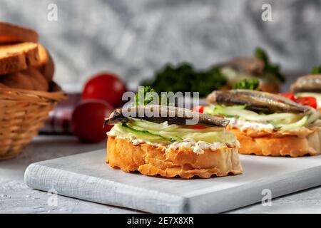 Geräuchertes Sprotte Sandwich - Fisch, frische Gurken und Tomaten. Sproat Sandwiches auf gerösteten Brotscheiben Stockfoto