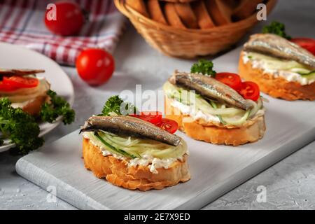 Geräuchertes Sprotte Sandwich - Fisch, frische Gurken und Tomaten. Sproat Sandwiches auf gerösteten Brotscheiben Stockfoto