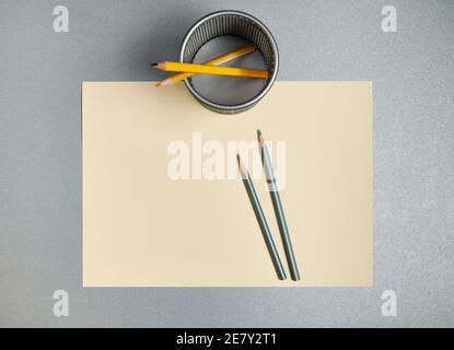 Bleistifte und Bleistifthalter auf gelbem Papier auf grauem Hintergrund. Flach liegend. Stockfoto