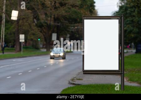 Vertikale leere Plakatwand auf der Stadtstraße, im Hintergrund die entkochte Abendstraße mit Autos Stockfoto