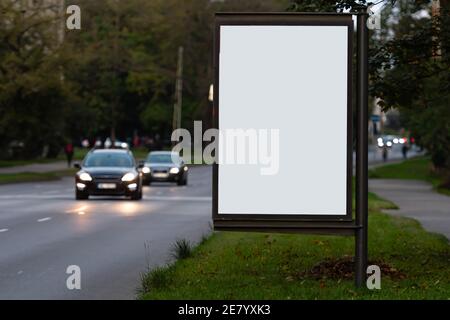 Vertikale leere Plakatwand auf der Stadtstraße, im Hintergrund die entkochte Abendstraße mit Autos Stockfoto