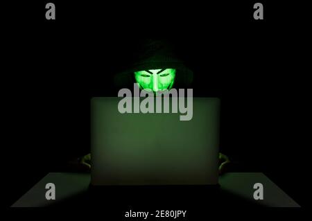 Mitglied der anonymen Hacker-Gruppe, die eine Maske vor seinem Laptop trägt, während sie einen Hack begeht. Stockfoto