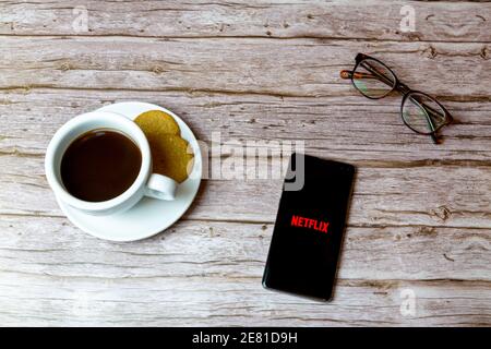 Ein Handy oder Handy auf einem Holz gelegt Tisch mit der Netflix App Öffnung auch einen Kaffee und Brille Stockfoto