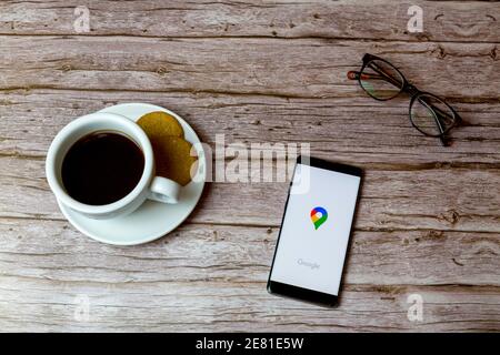 Ein Handy oder Handy auf einem Holz gelegt Tisch mit Google Maps App öffnen auch einen Kaffee und Brille Stockfoto