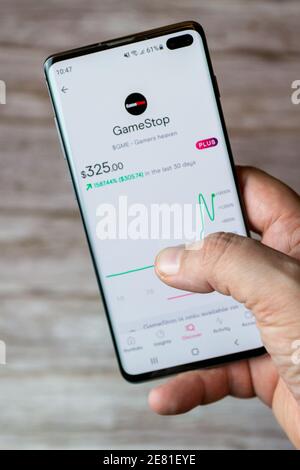 Eine Hand, die ein Mobiltelefon oder Mobiltelefon mit hält Die eine Trading-App auf dem Bildschirm geöffnet zeigt den Anstieg In Gamestop Stockfoto