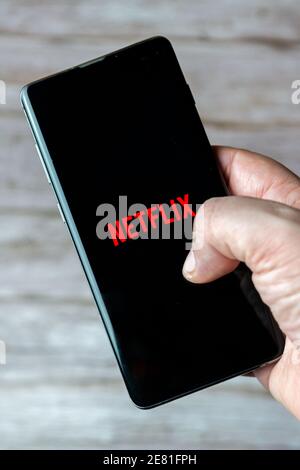 Eine Hand, die ein Mobiltelefon oder Mobiltelefon mit hält Netflix die App auf dem Bildschirm geöffnet Stockfoto