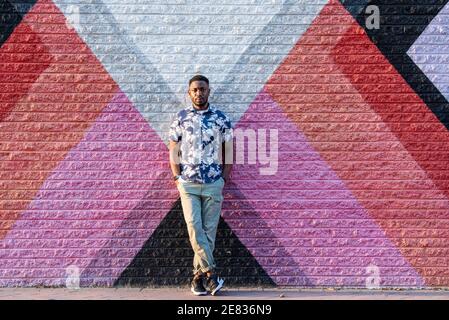 Ein schwarzer Mann lehnt sich an ein buntes Straßenbild und lächelt die Kamera an. Stockfoto