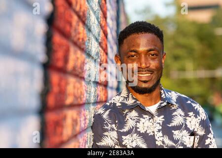 Ein schwarzer Mann lehnt sich an ein buntes Straßenbild und lächelt die Kamera an. Stockfoto