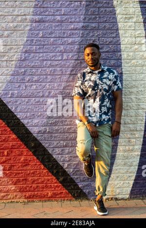 Ein schwarzer Mann lehnt sich an ein buntes Straßenbild und lächelt die Kamera an. Stockfoto