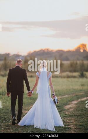 Vertikale Aufnahme eines Paares von hinten auf der Hochzeitstag mit Händen auf einem Feld Stockfoto