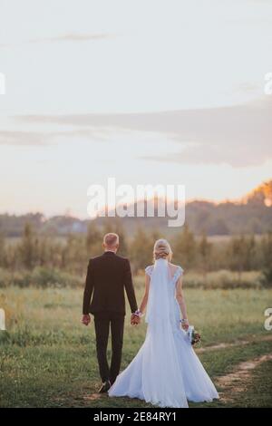 Vertikale Aufnahme eines Paares von hinten auf der Hochzeitstag mit Händen auf einem Feld Stockfoto