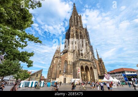 Ulm, Deutschland – 20. Juli 2019: Menschen gehen neben dem Ulmer Münster oder dem Ulmer Dom. Diese mittelalterliche Kirche ist ein berühmtes Wahrzeichen der Stadt. Landschaft von fa Stockfoto