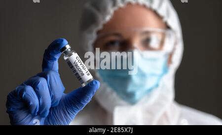 COVID-19-Impfstoff in der Hand des Arztes Nahaufnahme, Krankenschwester in der medizinischen persönlichen Schutzausrüstung (PSA) hält Flasche mit Impfstoff für Coronavirus Heilung. Konz Stockfoto