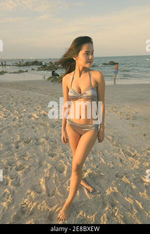 Junge schöne asiatische Frau denken beim Ständigen am öffentlichen Strand von Hua Hin in Thailand mit weichem Licht der Sonne strahlenden Stockfoto