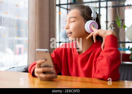 Teenager Mädchen hören die Musik über Kopfhörer und singen - Online-App im Handy. Modernes Technologiekonzept. Stockfoto