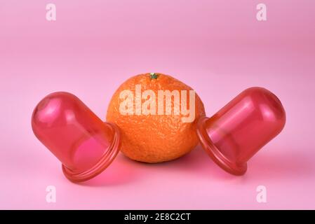 Zwei Massagegläser aus Silikon und eine Mandarine auf rosa Hintergrund, Anti-Cellulite und therapeutische Massageprodukte. Stockfoto