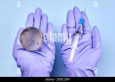 Die Hände der Frau in medizinischen Handschuhen halten einen Planeten Erde Globus und eine Spritze, das Konzept der Impfung. Stockfoto