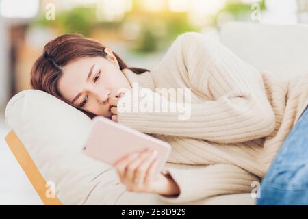 Gestresste junge Frau, die auf dem Sofa liegt und das Handy beobachtet Stockfoto