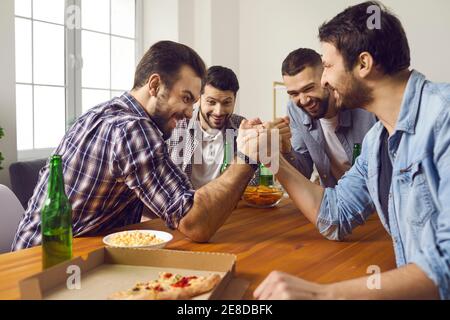 Gruppe von Freunden beobachten zwei Männer Arm-Wrestling auf Spaß Party Mit Pizza und Bier Stockfoto