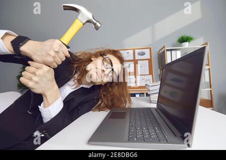Verärgerte Büroangestellte zerschlagen Laptop mit Hammer wegen des Ausfalls Oder Datenfehler Stockfoto
