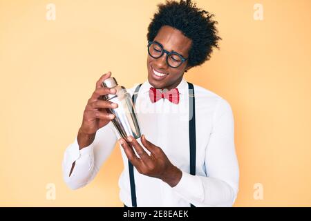 Hübscher afroamerikanischer Barkeeper mit Afro-Haar, der Cocktail zubereitet Mixing Drink mit Shaker lächelnd Blick auf die Seite und Wegstarren thinki Stockfoto