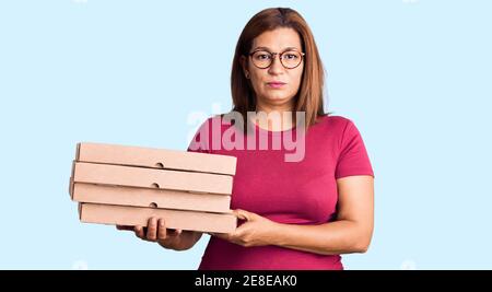 Mittelalter latina Frau hält Lieferung Pizza Box Denken Haltung Und nüchterner Ausdruck, der selbstbewusst aussieht Stockfoto