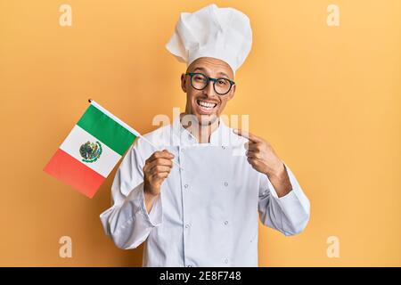 Glatze Mann mit Bart tragen professionelle Koch Schürze hält mexiko Flagge lächelnd glücklich zeigt mit Hand und Finger Stockfoto