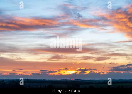 Sonnenaufgang über dem Südosten Kents mit der Sonne, die rot erscheint, durch schwere dunkle Wolken am Horizont mit gelb-blauem Himmel mit vielen Wolken darüber. Stockfoto